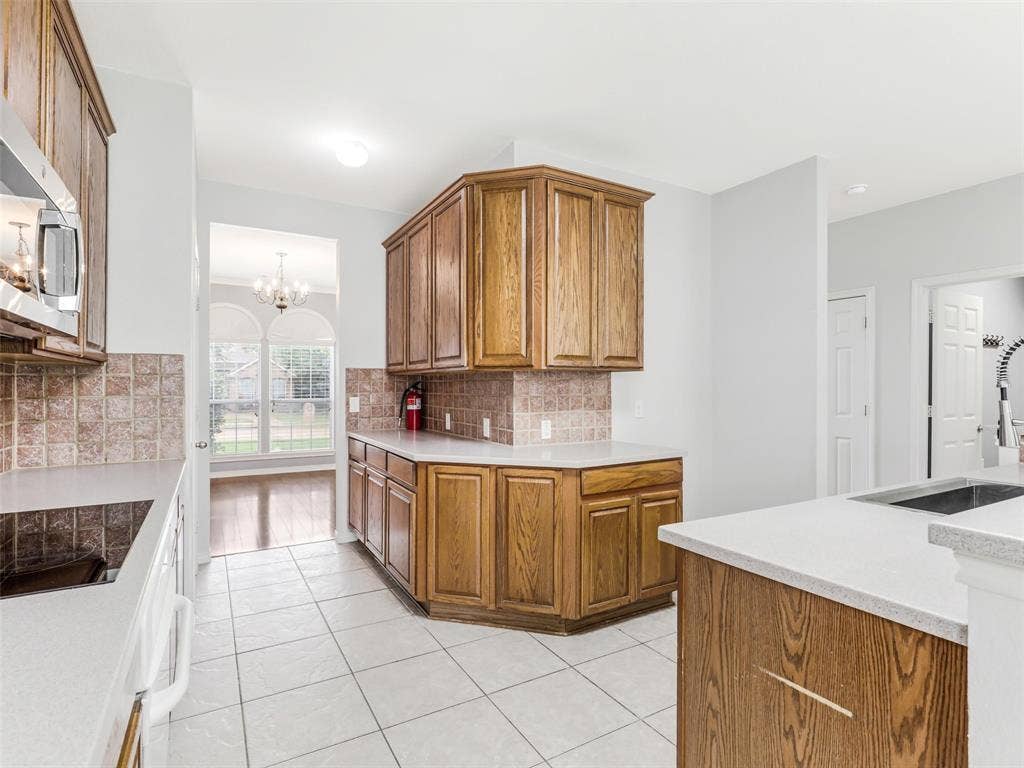 7419 Ravenhill Drive, Frisco, TX 75035 Kitchen featuring wood cabinetry, white countertops, tile flooring, and a tile backsplash