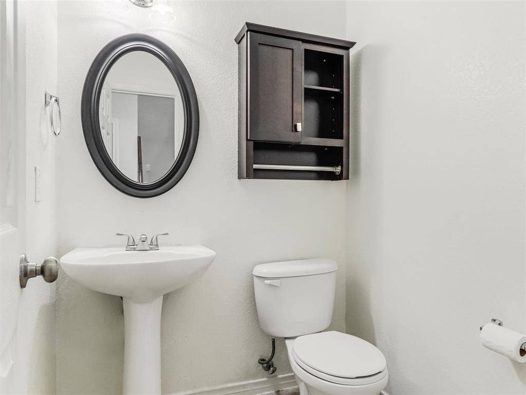 7419 Ravenhill Drive, Frisco, TX 75035 Pedestal sink with chrome-finish faucet, oval mirror, and wall-mounted storage cabinet