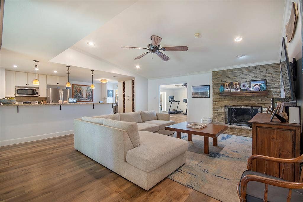 4074 Cedar Bayou Drive, Dallas, TX 75244 Open-concept living space featuring wood-finish flooring, a stacked stone fireplace, a kitchen with white cabinetry, and stainless steel appliances