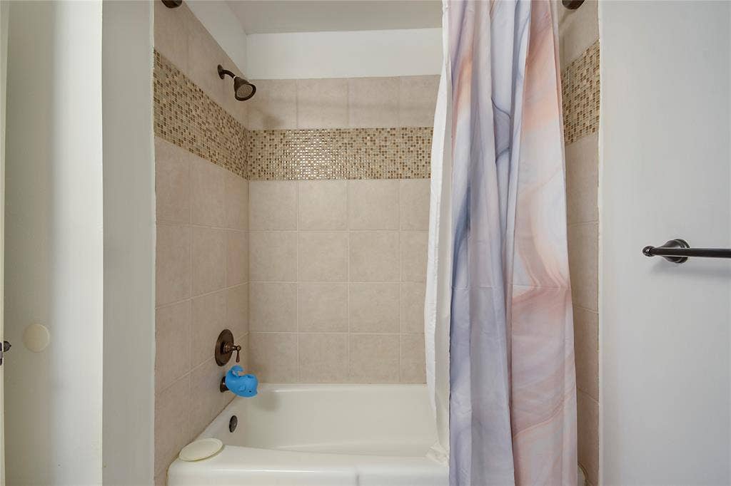 4074 Cedar Bayou Drive, Dallas, TX 75244 Bathtub with surrounding tile, decorative mosaic accent band, and bronze finish fixtures