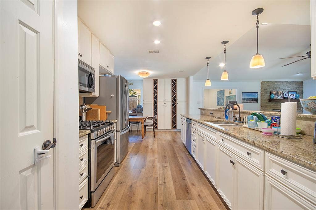 4074 Cedar Bayou Drive, Dallas, TX 75244 Galley kitchen with wood-finish flooring, white cabinetry, granite countertops, and stainless-steel appliances