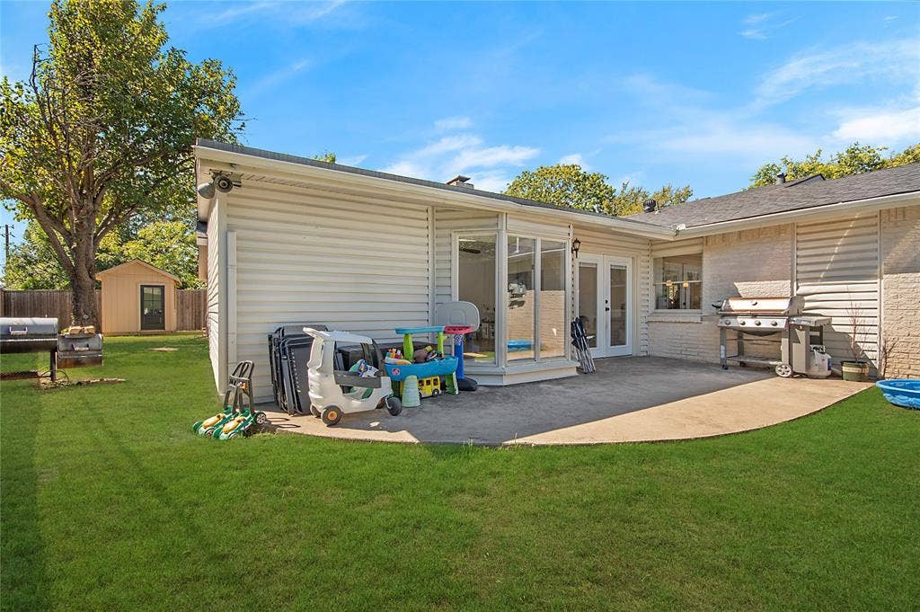 4074 Cedar Bayou Drive, Dallas, TX 75244 Expansive backyard with a manicured lawn, concrete patio, and a sunroom featuring full-light double doors