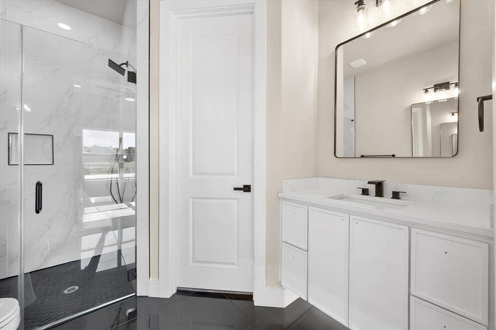 Glass-enclosed shower with a black tile floor, white tiled walls, and a recessed niche