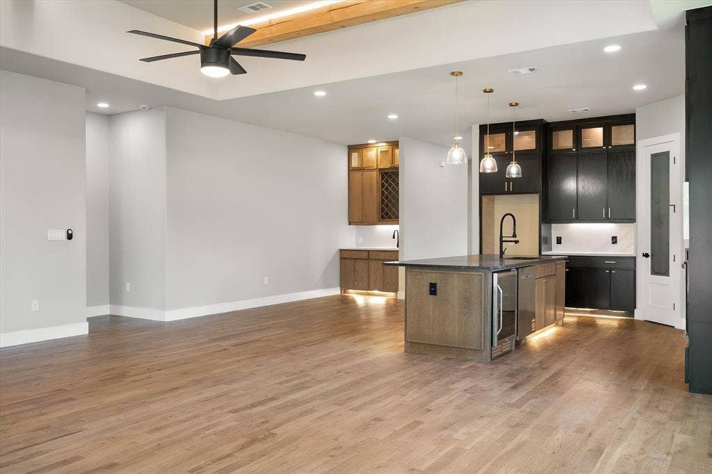 Wood-finish flooring throughout, tray ceiling with exposed wood beam, recessed lighting, and a modern ceiling fan