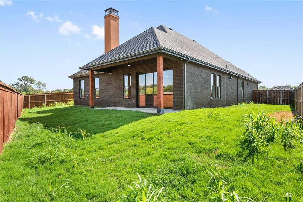 Brick exterior with a covered patio featuring wood columns, a shingled roof, and a privacy fence