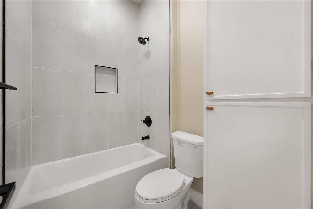 Bathtub with matte black fixtures, tiled surround, recessed shower niche, and adjacent built-in cabinetry