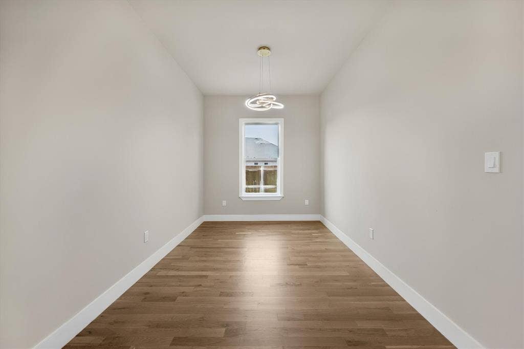Room featuring light-toned walls, wood-finish flooring, a contemporary pendant light fixture, and a window with white trim