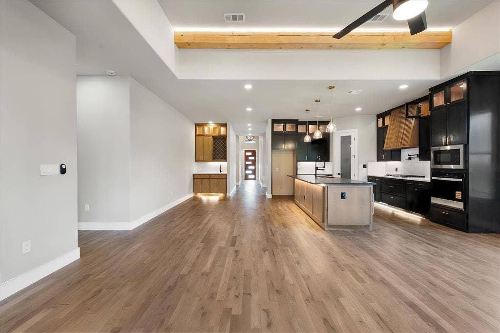Wide plank wood-finish flooring, recessed lighting, kitchen with stainless steel appliances, central kitchen island, and built-in cabinetry with under-cabinet lighting