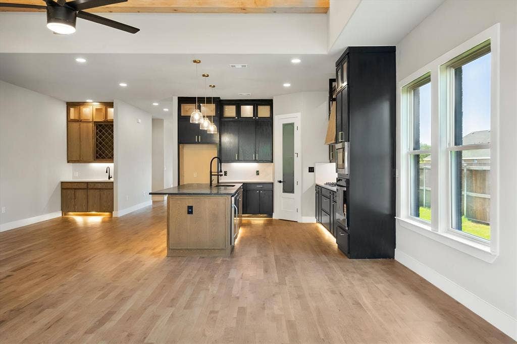 Wood-finish flooring throughout, featuring a kitchen island with pendant lighting, dark cabinetry, and a built-in beverage bar