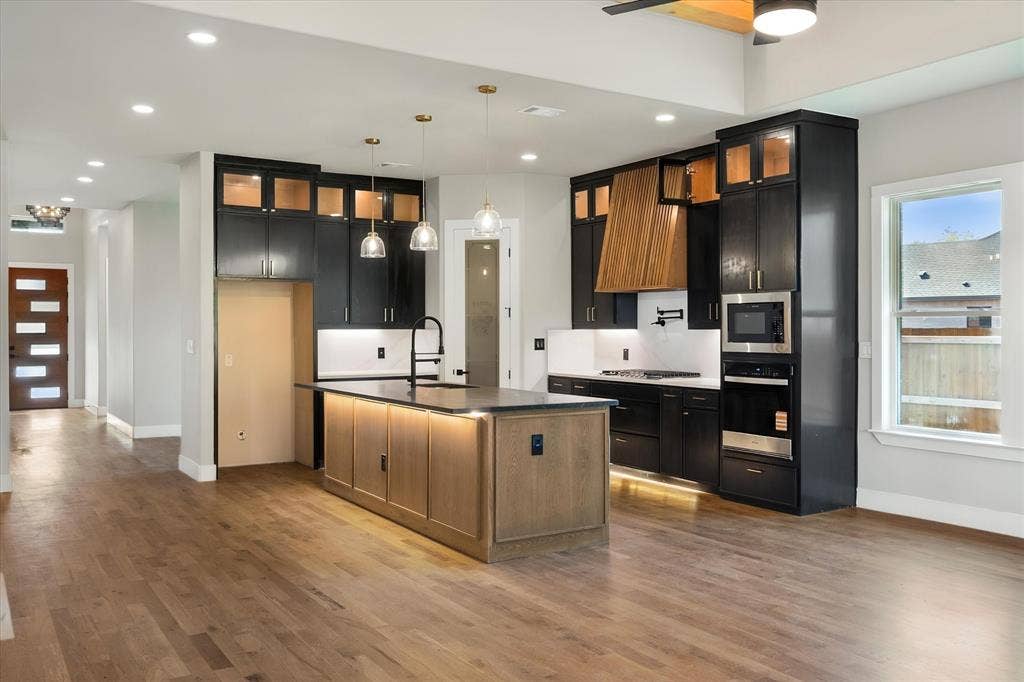 Kitchen featuring wood-finish flooring, a central island with integrated lighting, dark cabinetry, and built-in stainless steel appliances