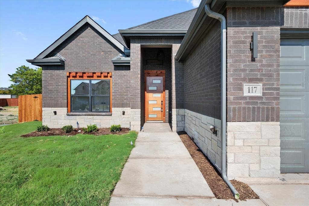 Dark brick exterior accented with light stone, contemporary wood-paneled entry door, sleek garage door, and a concrete walkway