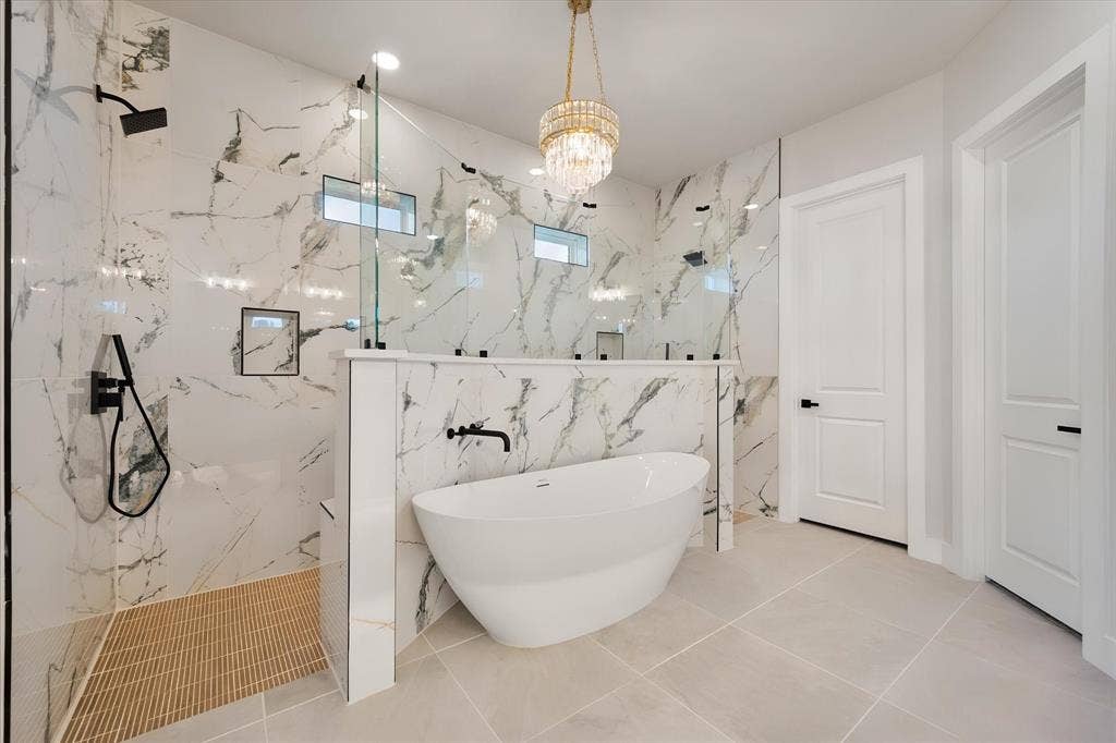 Spacious bathroom featuring a freestanding tub, large walk-in shower with glass enclosure, striking marble-look wall tile, and a decorative chandelier