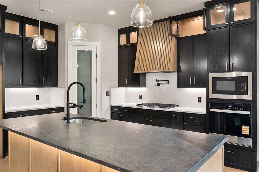 Kitchen featuring black cabinetry, light wood-finish accents, and integrated stainless steel appliances