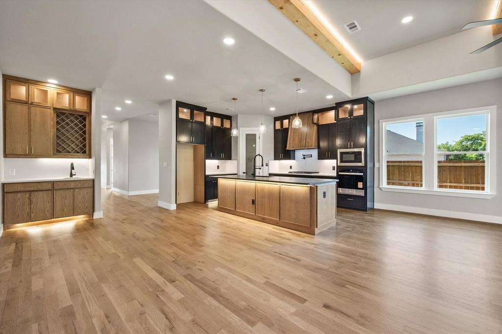 Open-concept living space with light wood-finish flooring, a kitchen island with pendant lighting, and a built-in beverage station