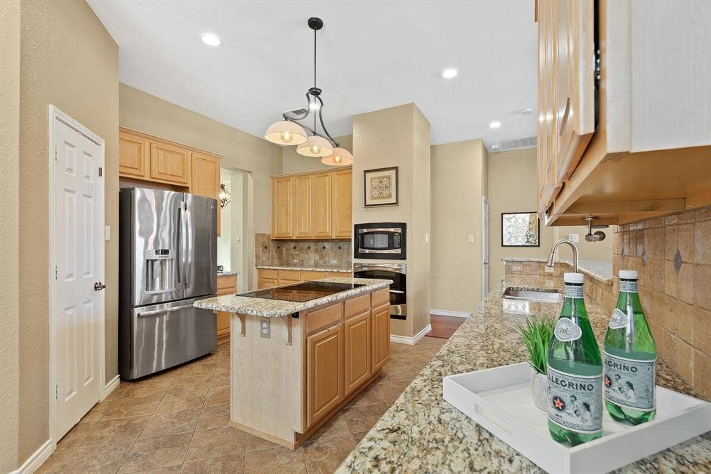 Kitchen featuring stainless steel appliances, granite countertops, wood cabinetry, tile flooring, and recessed lighting