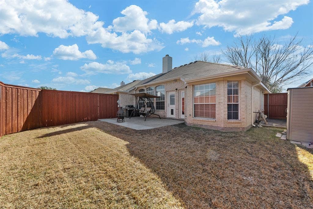 Expansive backyard featuring a privacy fence, concrete patio, and a light brick exterior with multiple windows