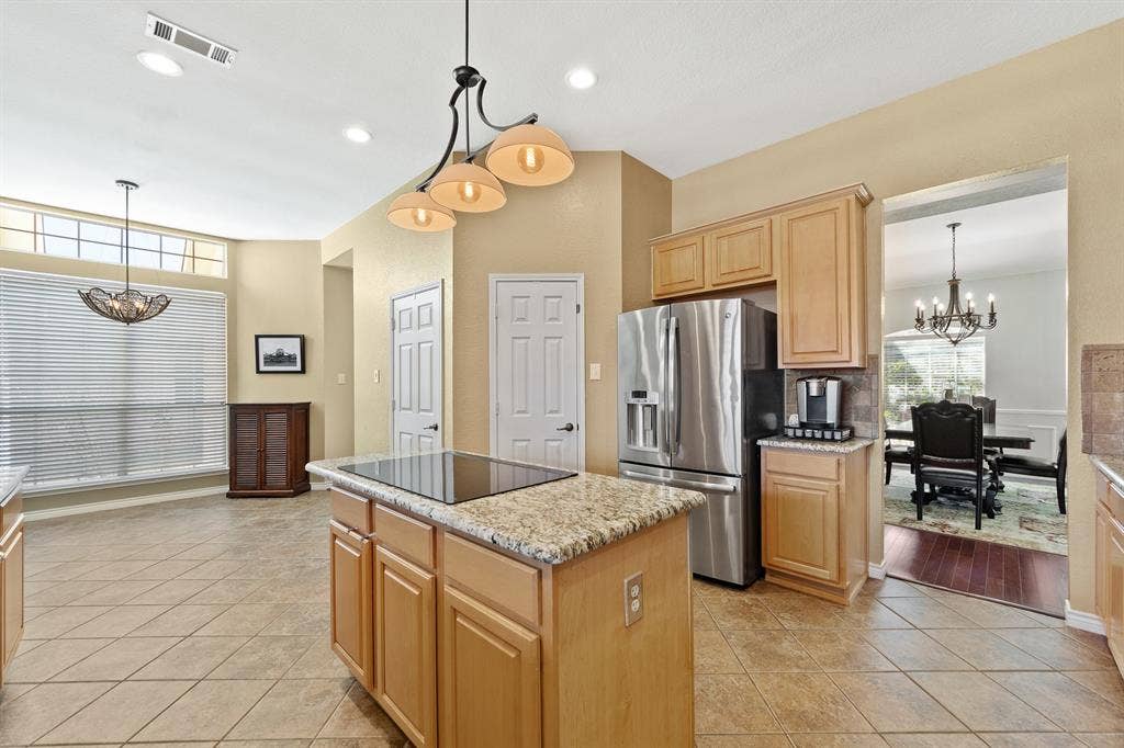 Kitchen featuring a central island with cooktop, stainless steel refrigerator, light-toned cabinetry, and tile flooring