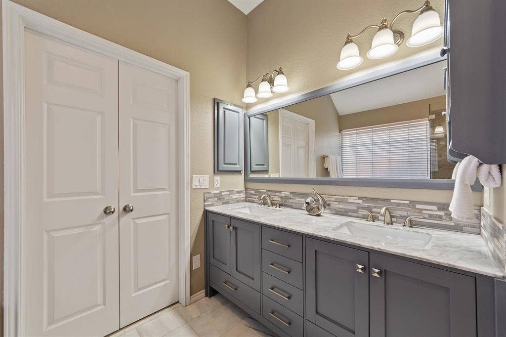 Dual vanity with gray cabinetry and brushed nickel hardware, white countertop, and mosaic tile backsplash