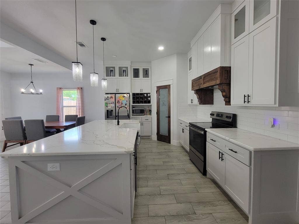 3207 NW 30th Street, Fort Worth, TX 76106 Spacious kitchen featuring an expansive center island with countertop, white shaker cabinetry, tiled flooring, built-in pantry door, and a built-in range with a wood-finished hood