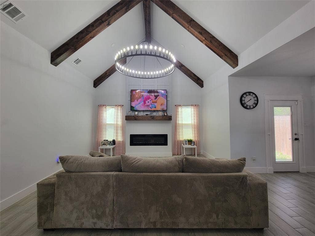 3207 NW 30th Street, Fort Worth, TX 76106 Vaulted ceiling with exposed wood beams, a contemporary chandelier, and a built-in electric fireplace with a wood-finish mantel