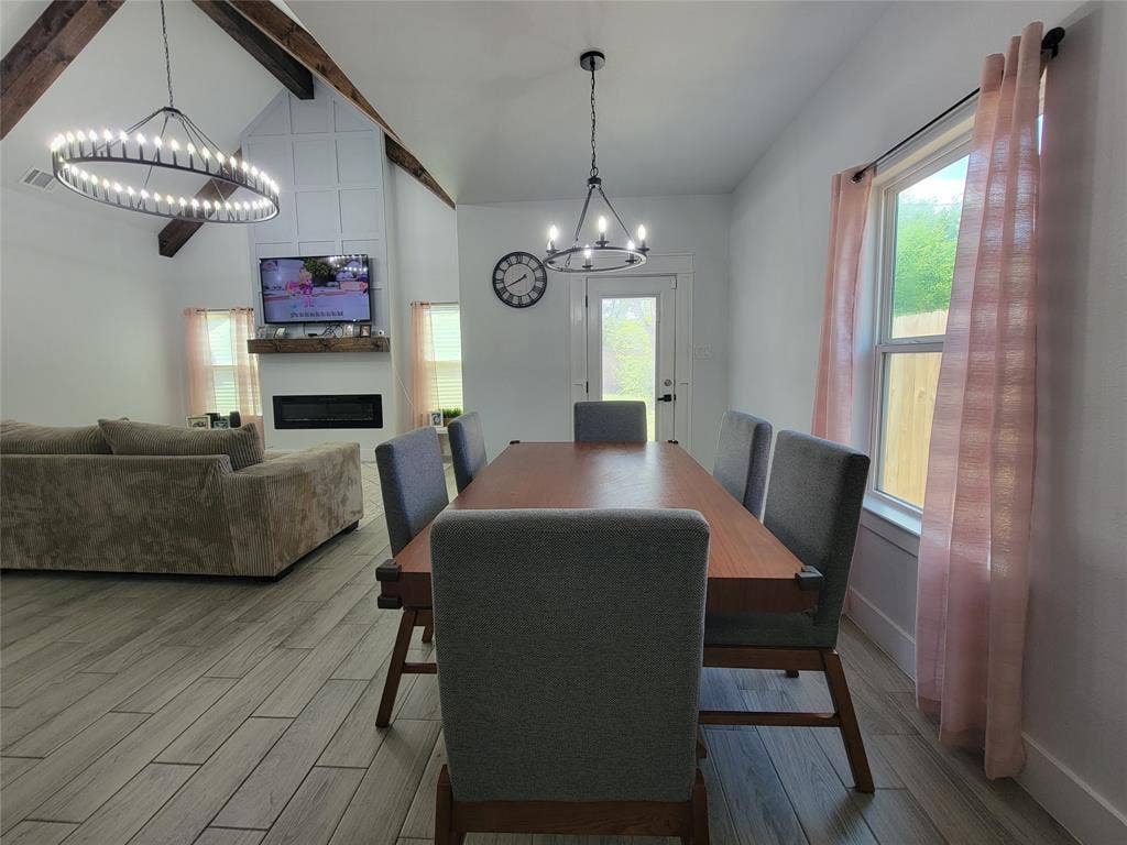 3207 NW 30th Street, Fort Worth, TX 76106 Vaulted ceiling with exposed wood beams, modern electric fireplace, wood-finish flooring, and contemporary light fixtures