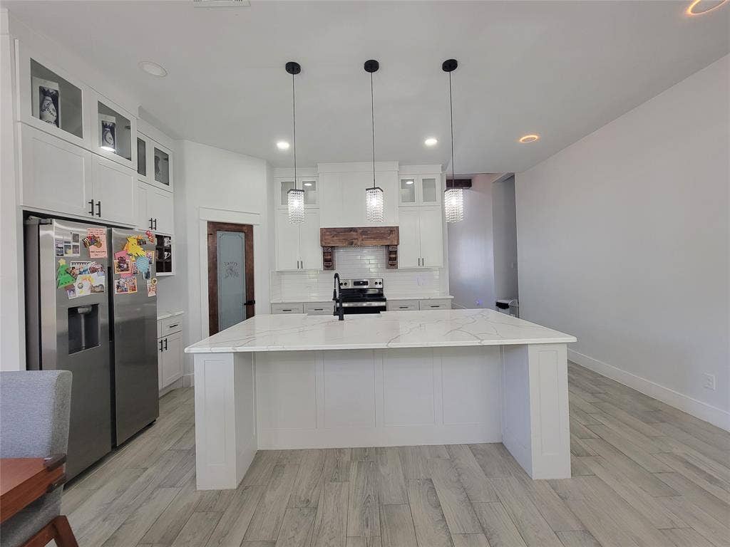 3207 NW 30th Street, Fort Worth, TX 76106 Spacious kitchen featuring a large central island with a light-toned countertop, white cabinetry with dark hardware, a tile backsplash, and light wood-finish flooring