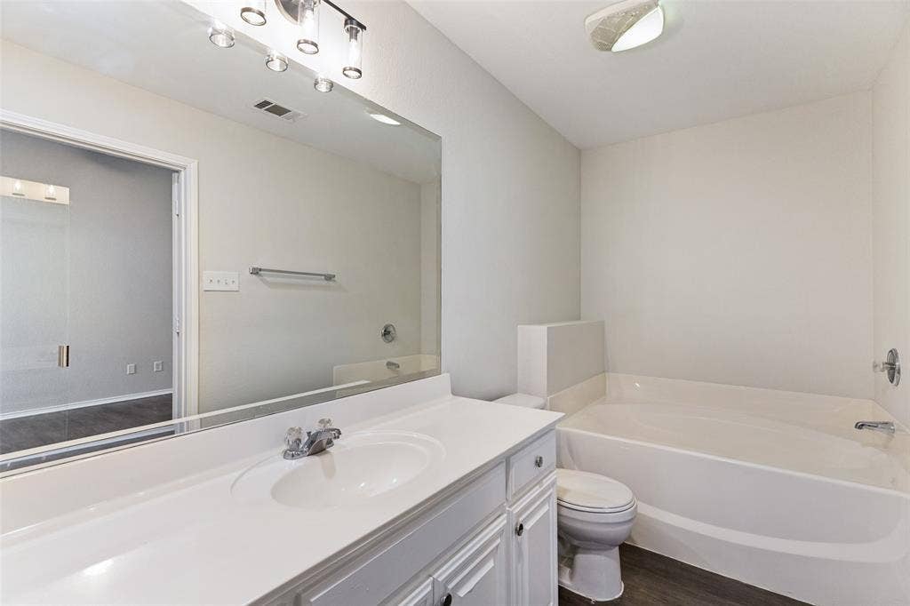 4545 Grainland Court, Fort Worth, TX 76179 White vanity with integrated sink, chrome faucet, large wall-mounted mirror, and white bathtub with chrome fixtures