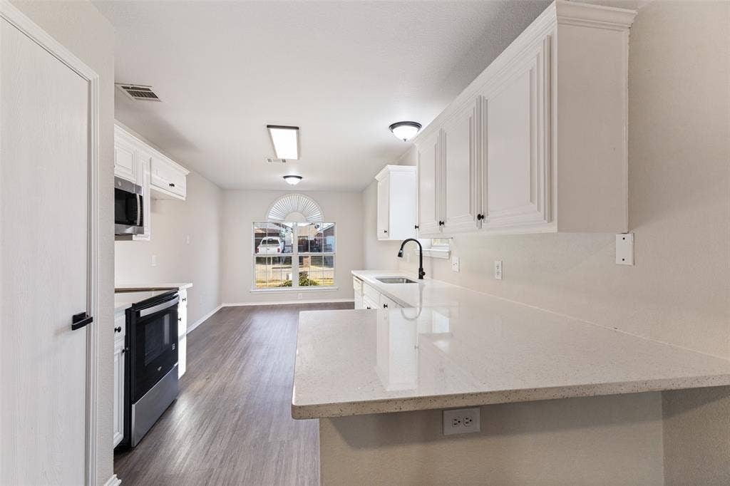 4545 Grainland Court, Fort Worth, TX 76179 White cabinetry with black hardware, light-toned countertops, wood-finish flooring, stainless steel appliances, and a rounded arch window