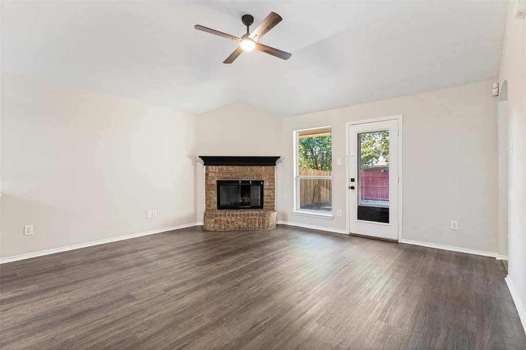 4545 Grainland Court, Fort Worth, TX 76179 Vaulted ceiling with a ceiling fan, brick fireplace with a dark mantle, wood-finish flooring, and a glass-paneled door