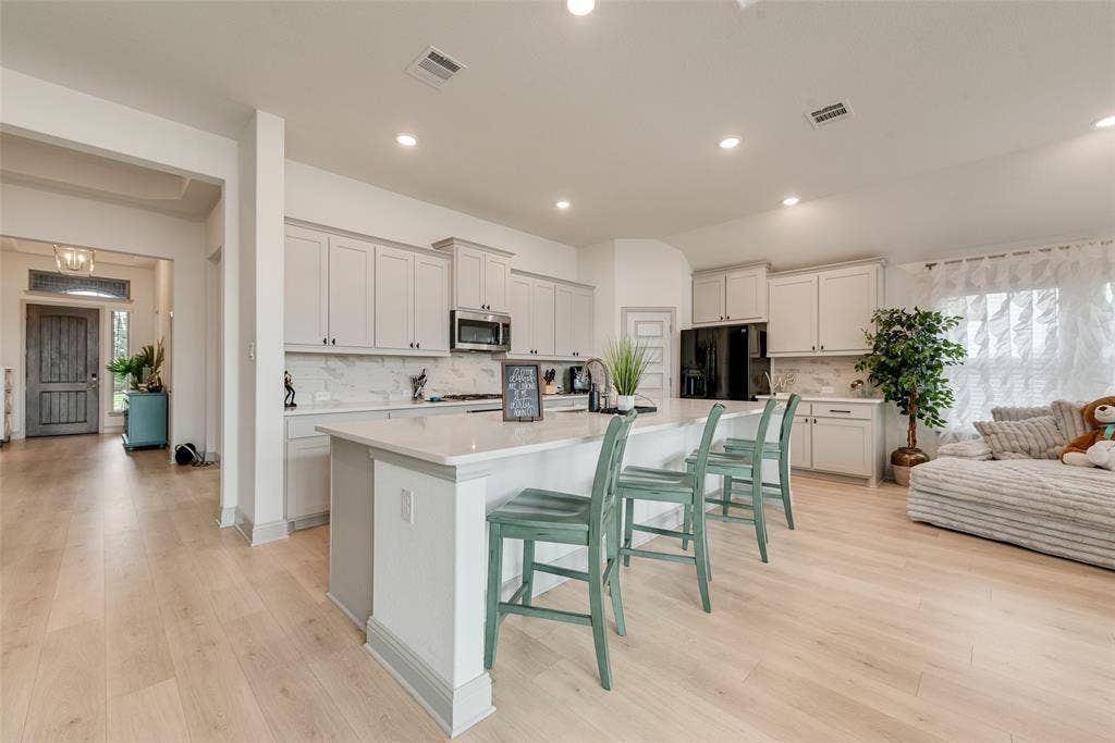107 White Sands Lane, Forney, TX 75126 Kitchen featuring light-toned cabinetry, a central island with countertop seating, stainless steel appliances, and wood-finish flooring