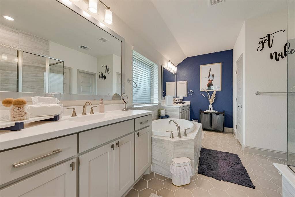 107 White Sands Lane, Forney, TX 75126 Dual-sink vanity with light gray cabinetry and white countertops, alongside a soaking tub