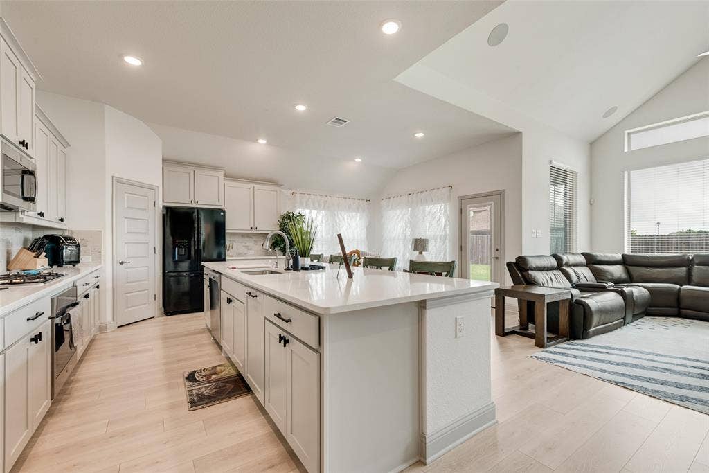 107 White Sands Lane, Forney, TX 75126 Recessed lighting, wood-finish flooring, white cabinetry with dark hardware, kitchen island with integrated sink, and vaulted ceiling