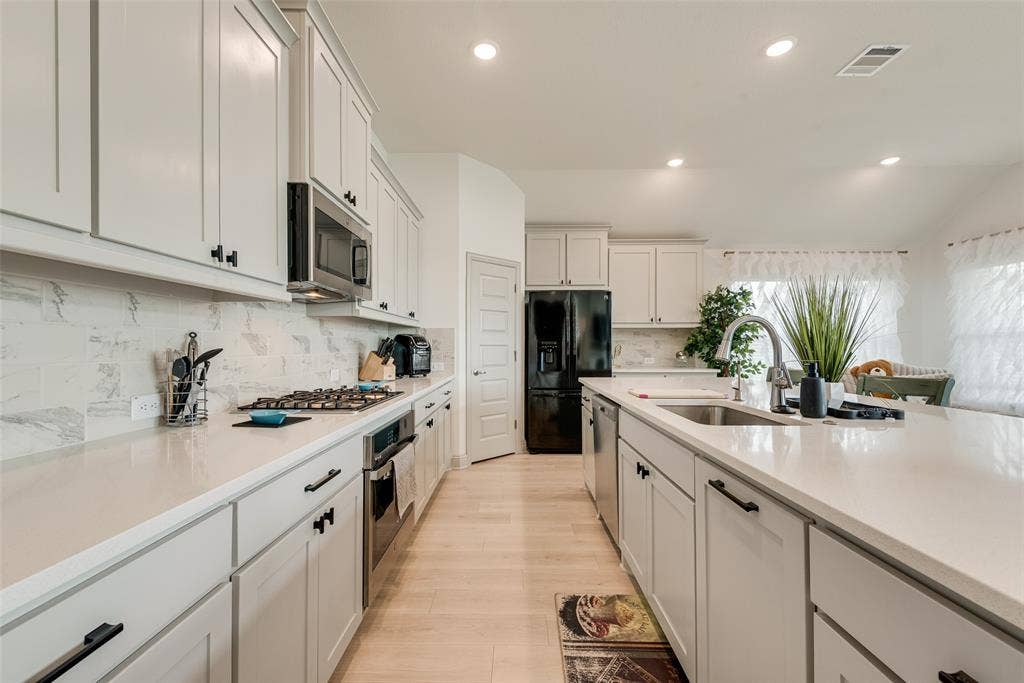 107 White Sands Lane, Forney, TX 75126 Kitchen featuring extensive light-toned cabinetry with matte black hardware, integrated stainless steel appliances, light-toned countertops, and a full-height tile backsplash