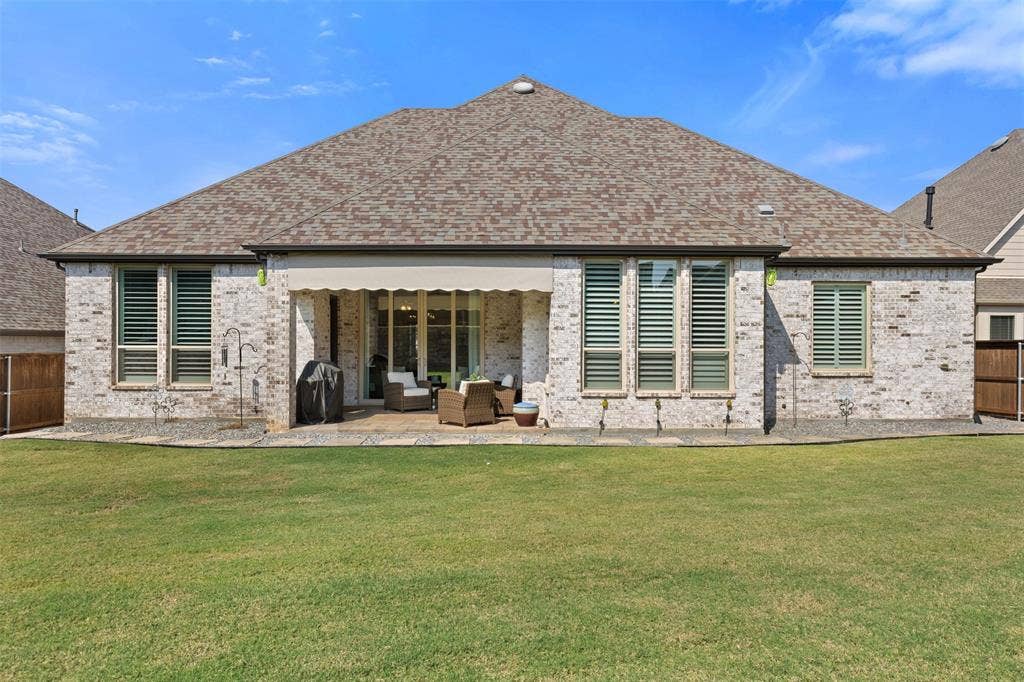 9716 Wilderness Road, Little Elm, TX 75068 Expansive backyard with a covered patio, featuring a retractable awning, stone paver patio, and a manicured lawn