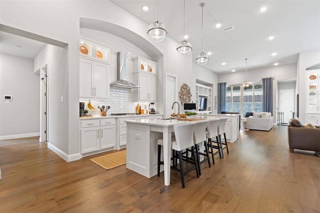 9716 Wilderness Road, Little Elm, TX 75068 Open-concept living space featuring wood-finish flooring, a white kitchen island with counter seating, pendant lighting, recessed lighting, and white cabinetry