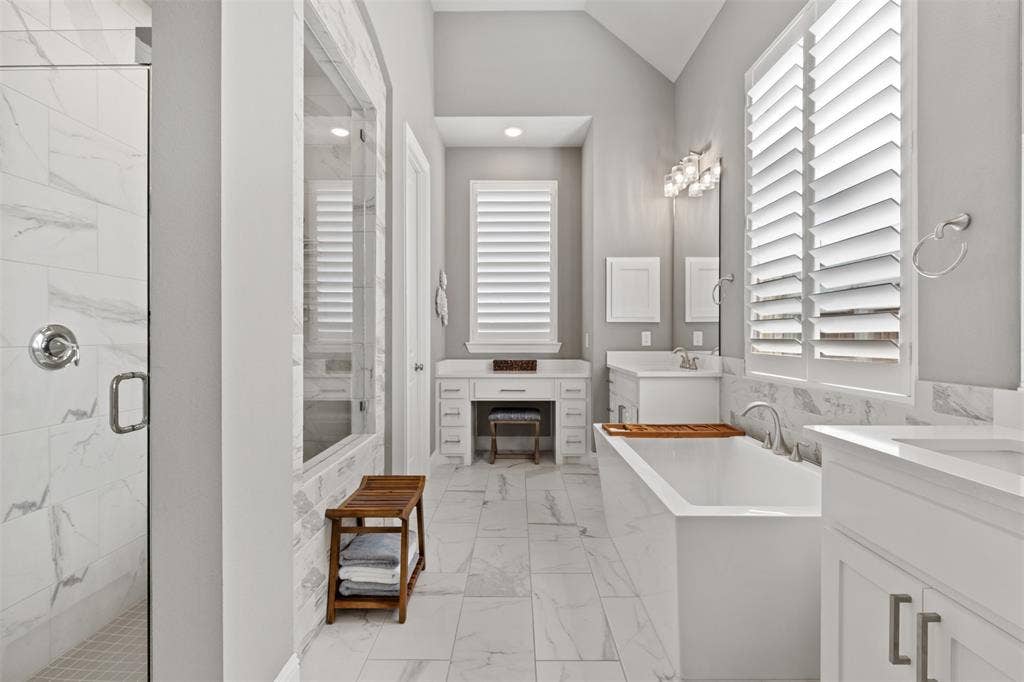 9716 Wilderness Road, Little Elm, TX 75068 Primary bathroom featuring walk-in shower with clear glass enclosure, freestanding soaking tub, dual vanity with and plantation shutters