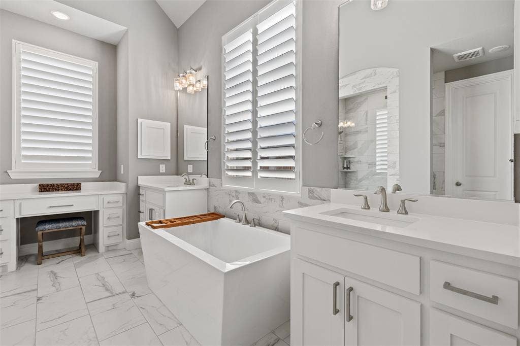 9716 Wilderness Road, Little Elm, TX 75068 Freestanding soaking tub, dual vanity with undermount sinks, white cabinetry with brushed nickel hardware, expansive vanity counter space, and plantation shutters