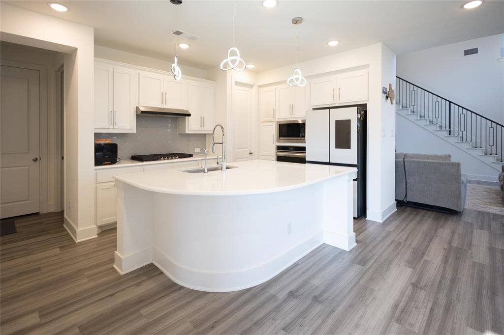 3017 Andorra Road, McKinney, TX 75071 Modern kitchen featuring a curved island, white cabinetry, integrated stainless steel appliances, and wood-finish flooring