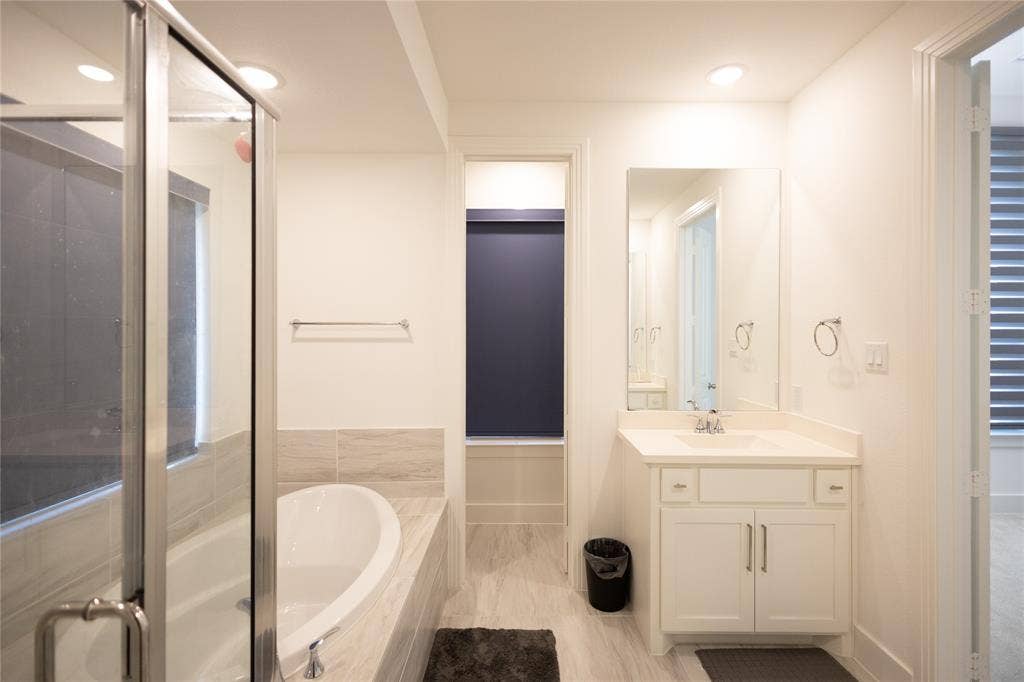 3017 Andorra Road, McKinney, TX 75071 Shower with glass enclosure, separate soaking tub, single vanity with integrated sink, rectangular mirror, and light-toned flooring