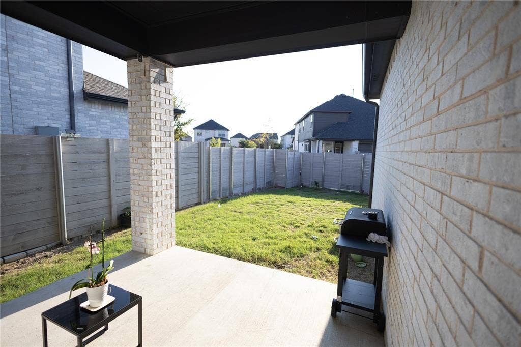 3017 Andorra Road, McKinney, TX 75071 Covered patio with a concrete slab, featuring a light-colored brick column and an expansive grass area