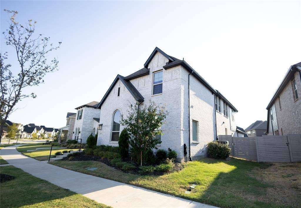3017 Andorra Road, McKinney, TX 75071 White brick exterior featuring a dark asphalt shingle roof, arched window, and landscaped front yard