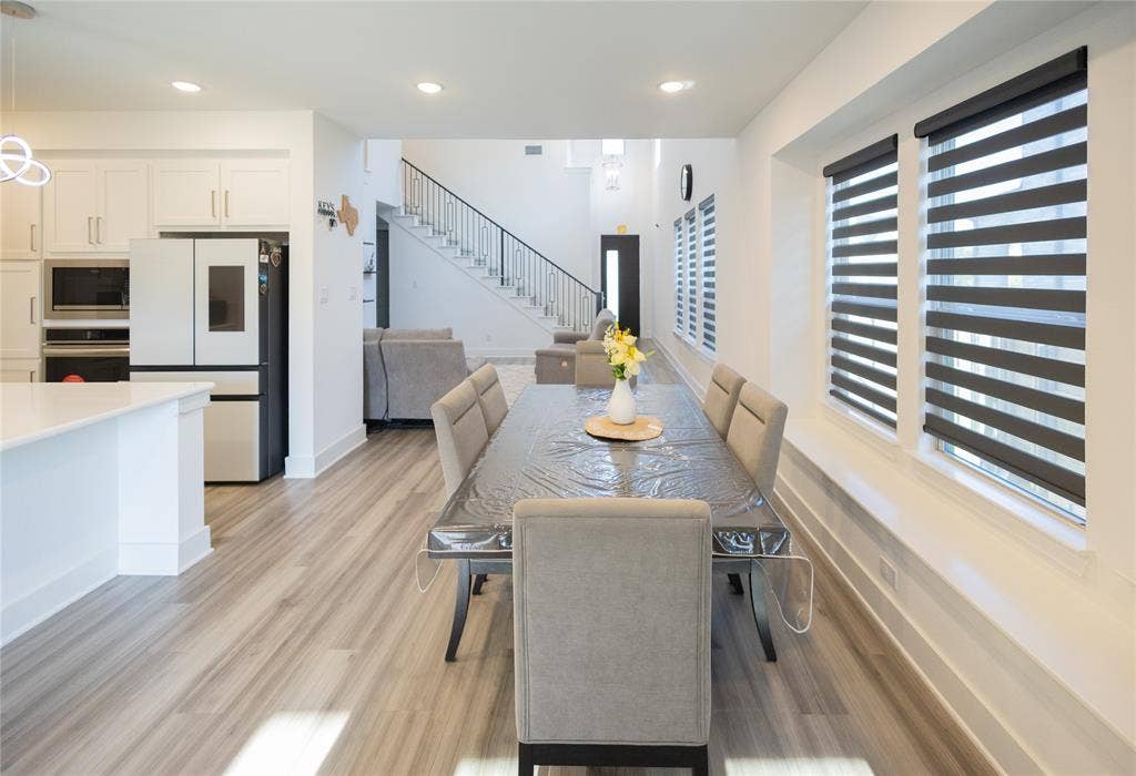 3017 Andorra Road, McKinney, TX 75071 Open-concept dining area with wood-finish flooring, white walls, and multiple windows featuring roller blinds