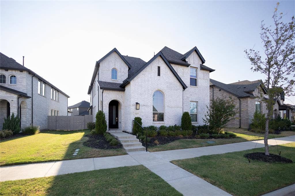 3017 Andorra Road, McKinney, TX 75071 White brick exterior with dark trim, arched entry, arched window, established landscaping, and concrete walkway