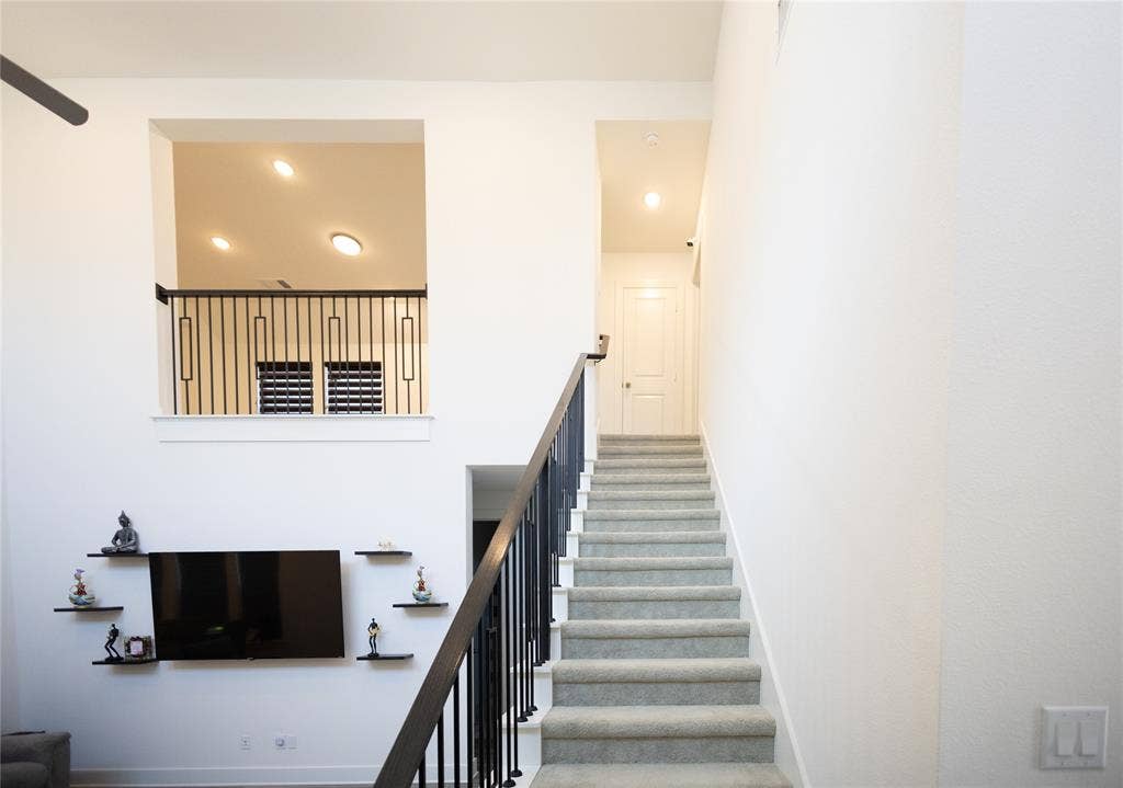 3017 Andorra Road, McKinney, TX 75071 Carpeted staircase with dark handrail and balusters, featuring a second-story interior balcony with matching balusters and recessed lighting