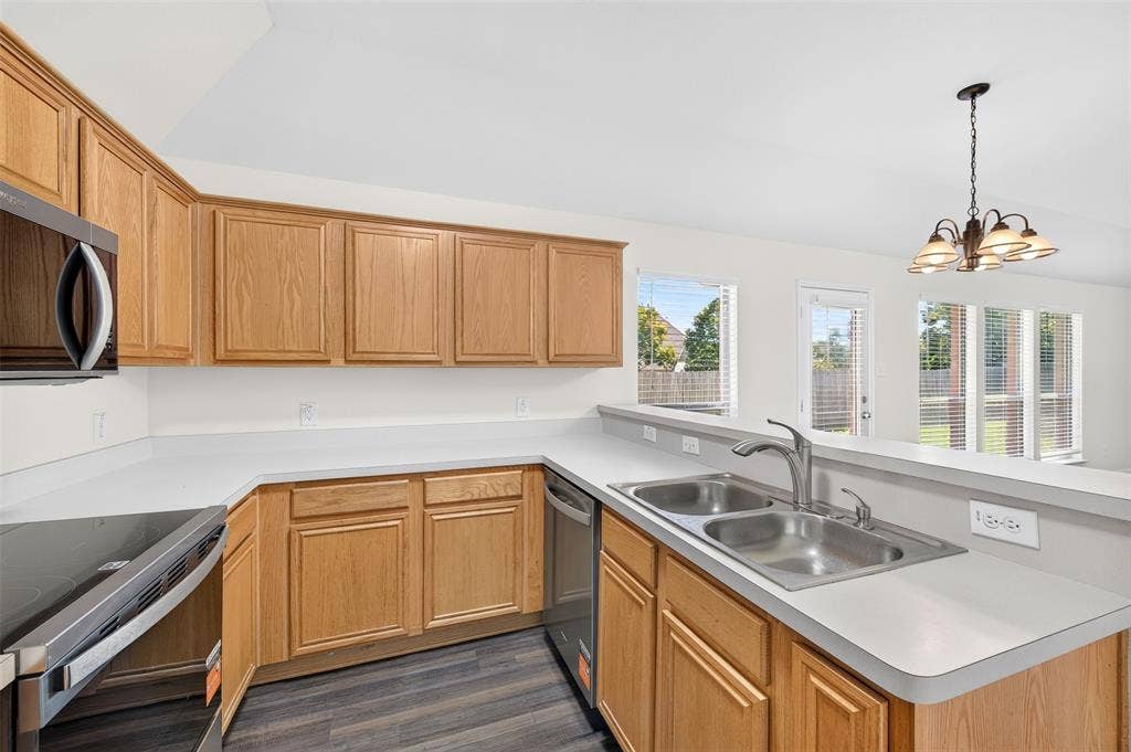 2724 Douglas Drive, McKinney, TX 75071 U-shaped kitchen with light wood cabinetry, light countertops, stainless steel sink, appliances and LVP flooring