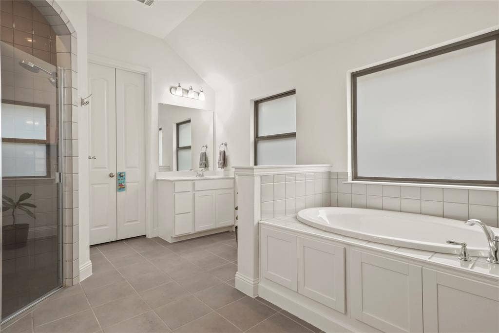 6152 Cobbetts Pond Lane, Fort Worth, TX 76179 Spacious bathroom featuring an oval soaking tub with tile surround, a glass-enclosed shower with tile walls, a single vanity with storage, and grey tile flooring