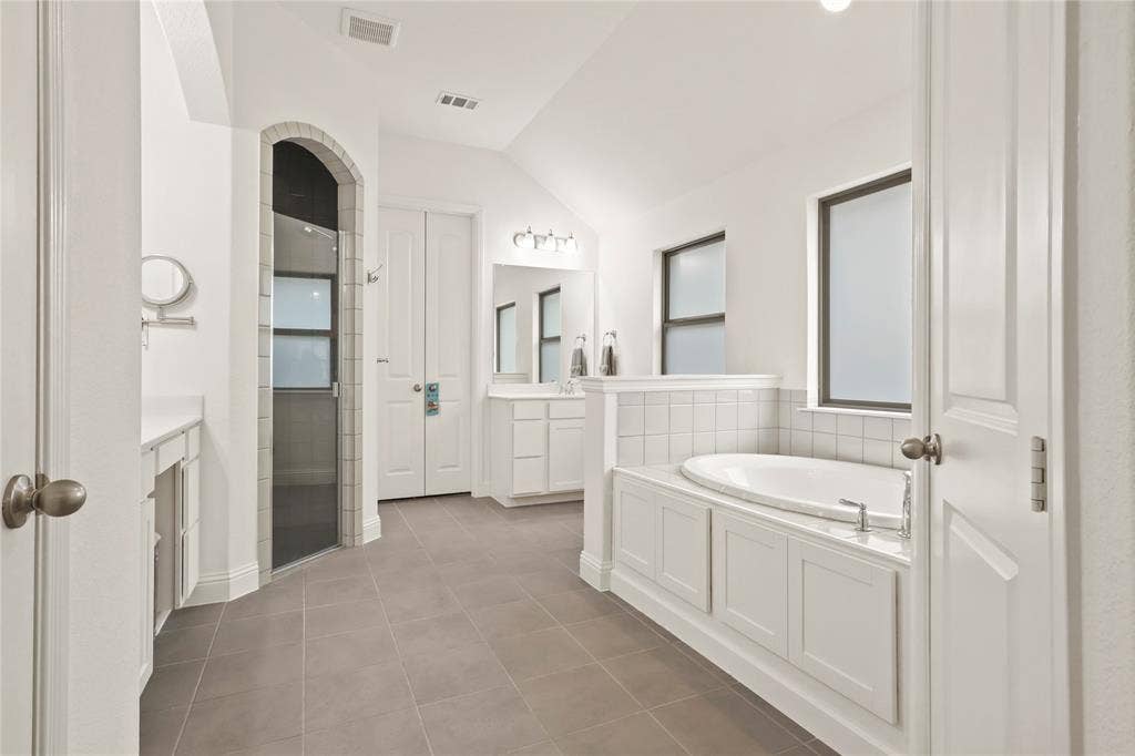 6152 Cobbetts Pond Lane, Fort Worth, TX 76179 Spacious bathroom with neutral tile flooring, built-in soaking tub, separate arched shower, and dual vanities with integrated sinks