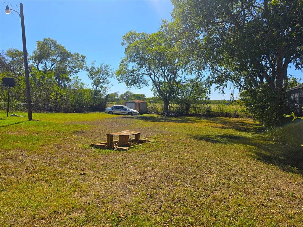 610 S Falls Street, Mart, TX 76664 Expansive grassy area with mature trees, featuring a wooden picnic table and a storage shed