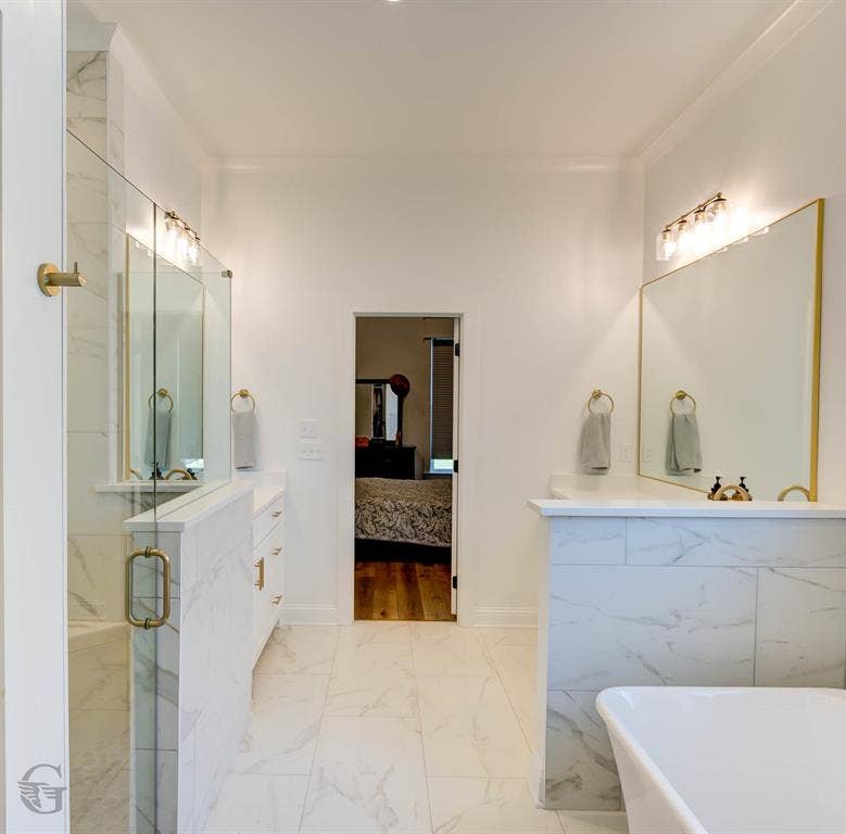 Bathroom featuring large-format tile flooring, a glass-enclosed shower with brass hardware, a vanity with white cabinetry, a freestanding bathtub, and a framed vanity mirror