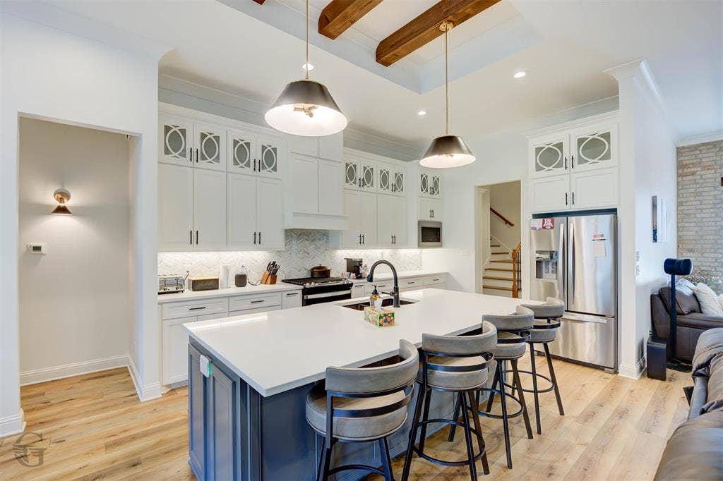 Kitchen featuring a central island with countertop seating, white cabinetry with decorative glass accents, wood-finish flooring, and exposed ceiling beams
